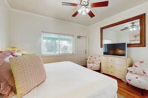 A bedroom with a bed, a television, a ceiling fan, a window, and a door. - El Cerrito Place - Rooftop Deck & Historic Charm (Port Aransas)