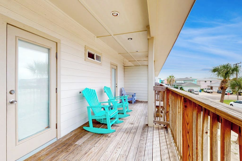 A covered porch with wooden flooring, a railing, and turquoise rocking chairs.