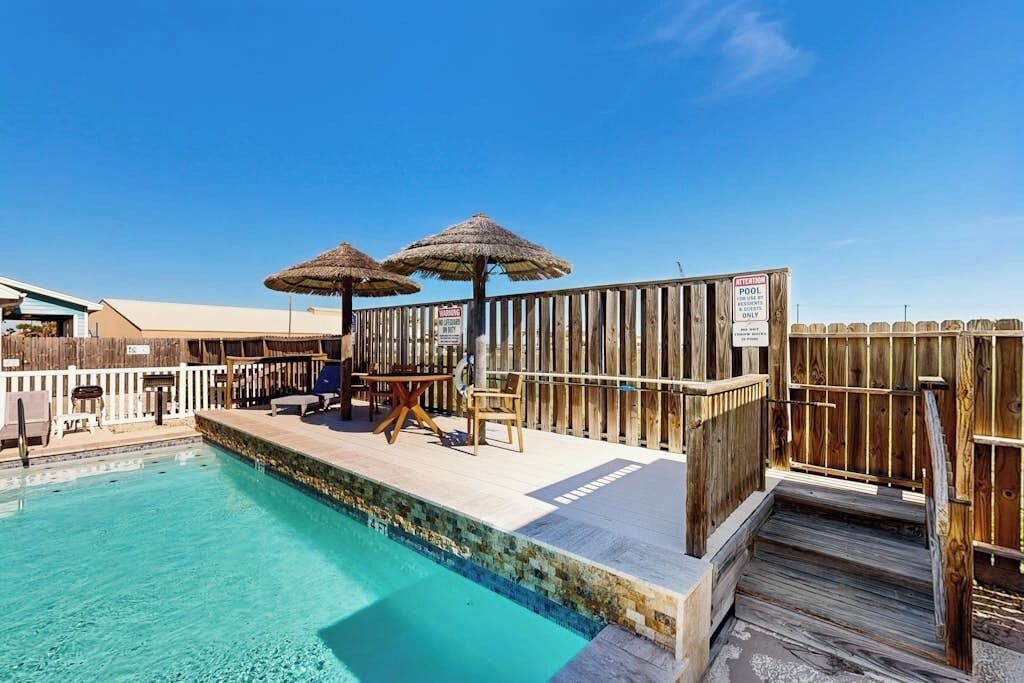 A pool area with a wooden deck, two umbrellas, and a sign indicating it's a private pool.