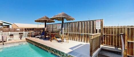 Uma área de piscina com um deck de madeira, dois guarda-sóis e um aviso indicando ser uma piscina privativa.