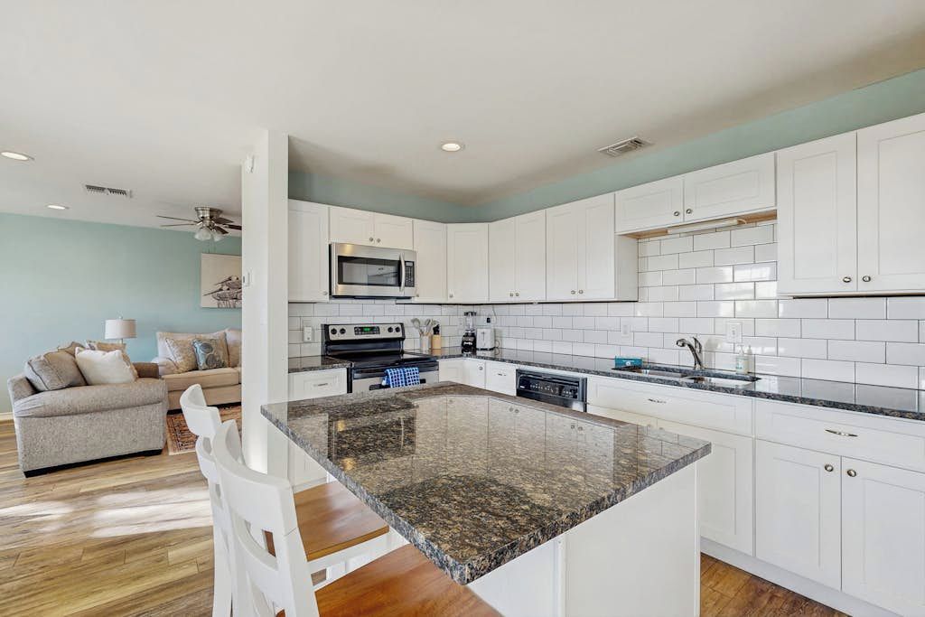 A modern kitchen with white cabinets, a granite countertop, and a built-in microwave.
