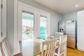 A dining area with a glass table and chairs, a stainless steel refrigerator, and a view through a window. - Heron's Hideaway - Screened Porch, Walk to Bay (Rockport)