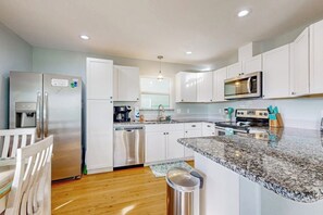 A modern kitchen with stainless steel appliances, white cabinetry, and a granite countertop. - Heron's Hideaway - Screened Porch, Walk to Bay (Rockport)