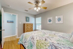 A bedroom with a bed, a ceiling fan, a wooden dresser, and two framed pictures on the wall. - Heron's Hideaway - Screened Porch, Walk to Bay (Rockport)