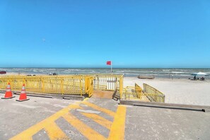 Uma praia com guarda-corpo amarelo, uma bandeira vermelha e céu azul límpido.