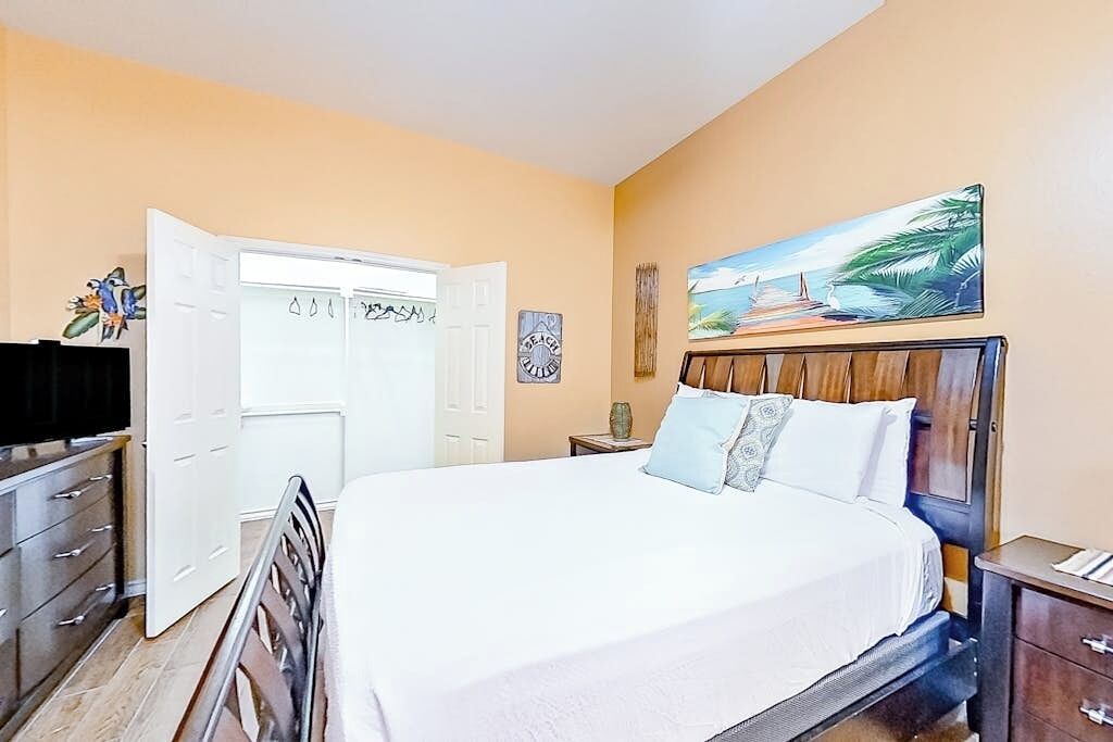 A bedroom with a bed, a wardrobe, a television, and a painting on the wall.