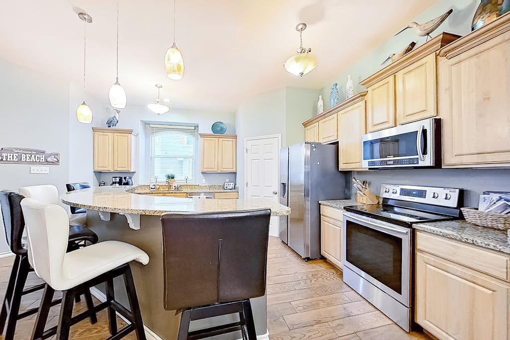 A kitchen with a central island, bar stools, stainless steel appliances, and pendant lighting.