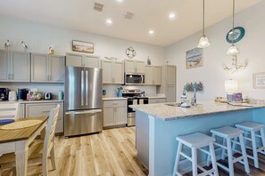A modern kitchen with stainless steel appliances, a central island with bar stools, and decorative wall art. - Sunshine Paradise - Water Views, Pool & Big Patio (Rockport)