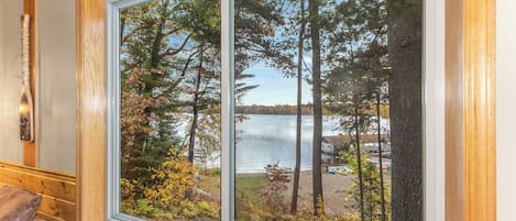 A room with a large window overlooking a lake and forest.