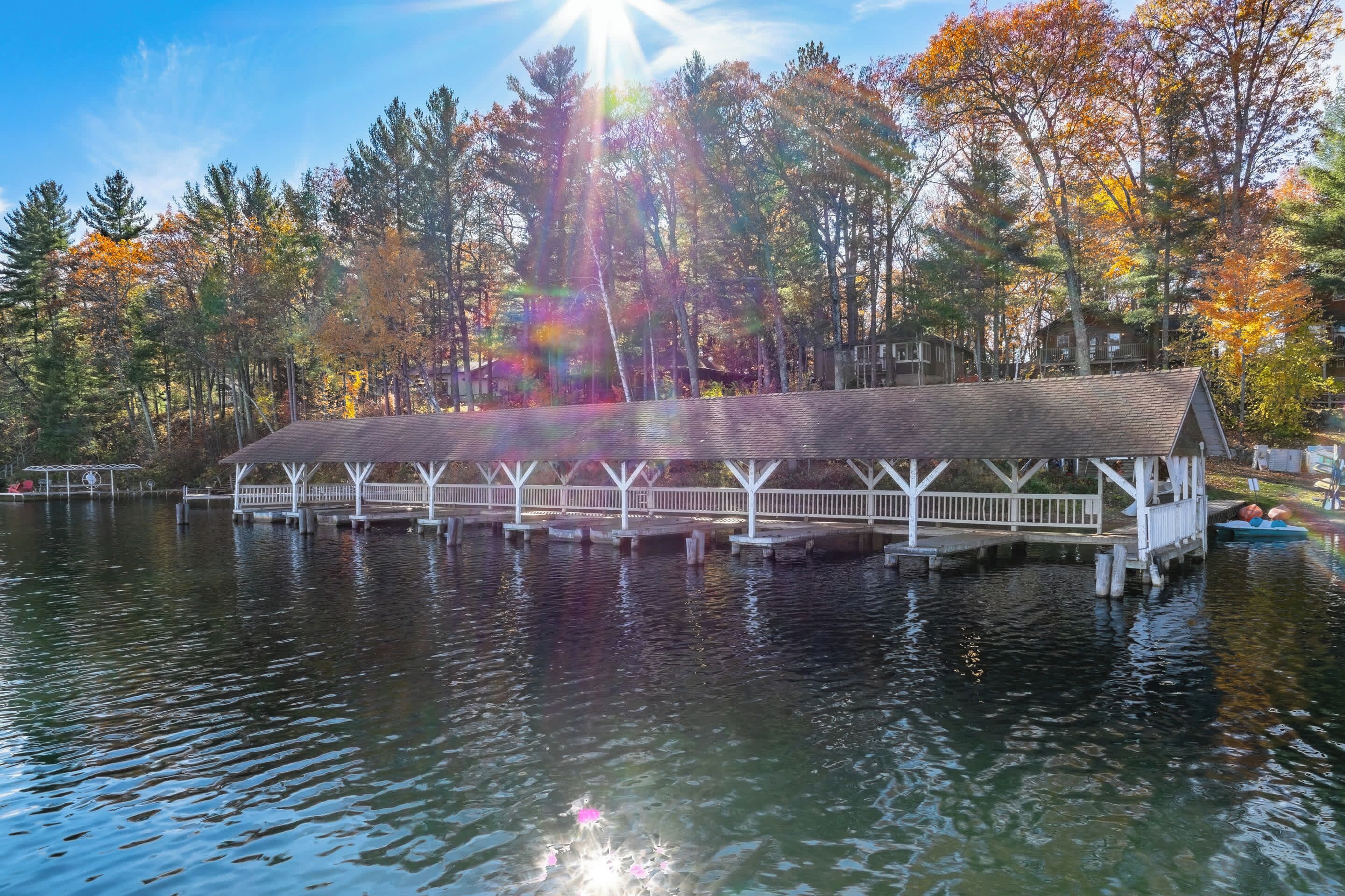 A covered dock extending into a calm lake, surrounded by trees with autumn foliage.