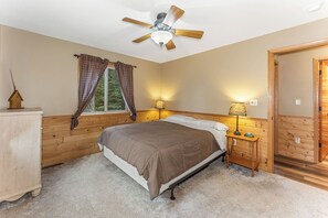 Quarto com cama, ventoinha no teto, janela com cortinas, abajur e guarda-roupa de madeira.