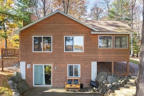 A two-story wooden cabin with a deck, a bench, and a grill area.