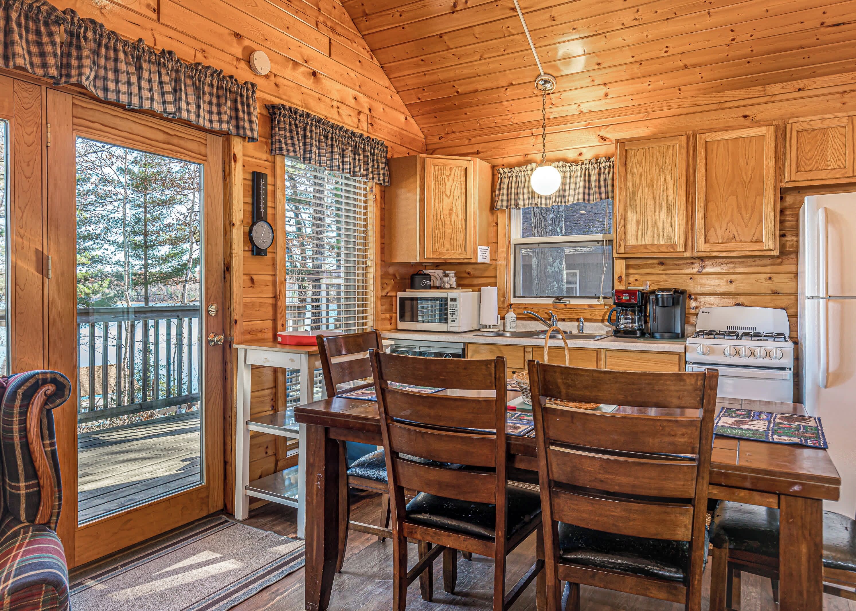 A wooden cabin interior with a dining area, kitchen, and a view of the outdoors.