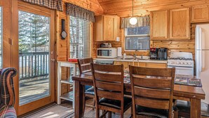 Interior de una cabaña de madera con comedor, cocina y vistas al exterior.