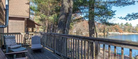 A wooden deck with outdoor seating and a view of a lake surrounded by trees.