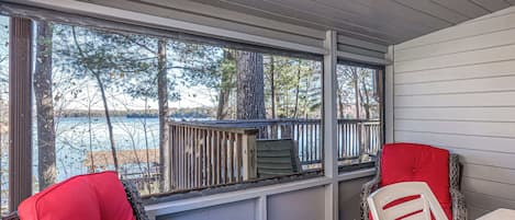 A covered outdoor seating area with wicker chairs and a table, overlooking a body of water and trees.