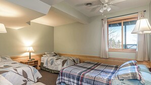 Un dormitorio con dos camas, un ventilador de techo, una ventana con cortinas y una mesita de noche con lámpara.