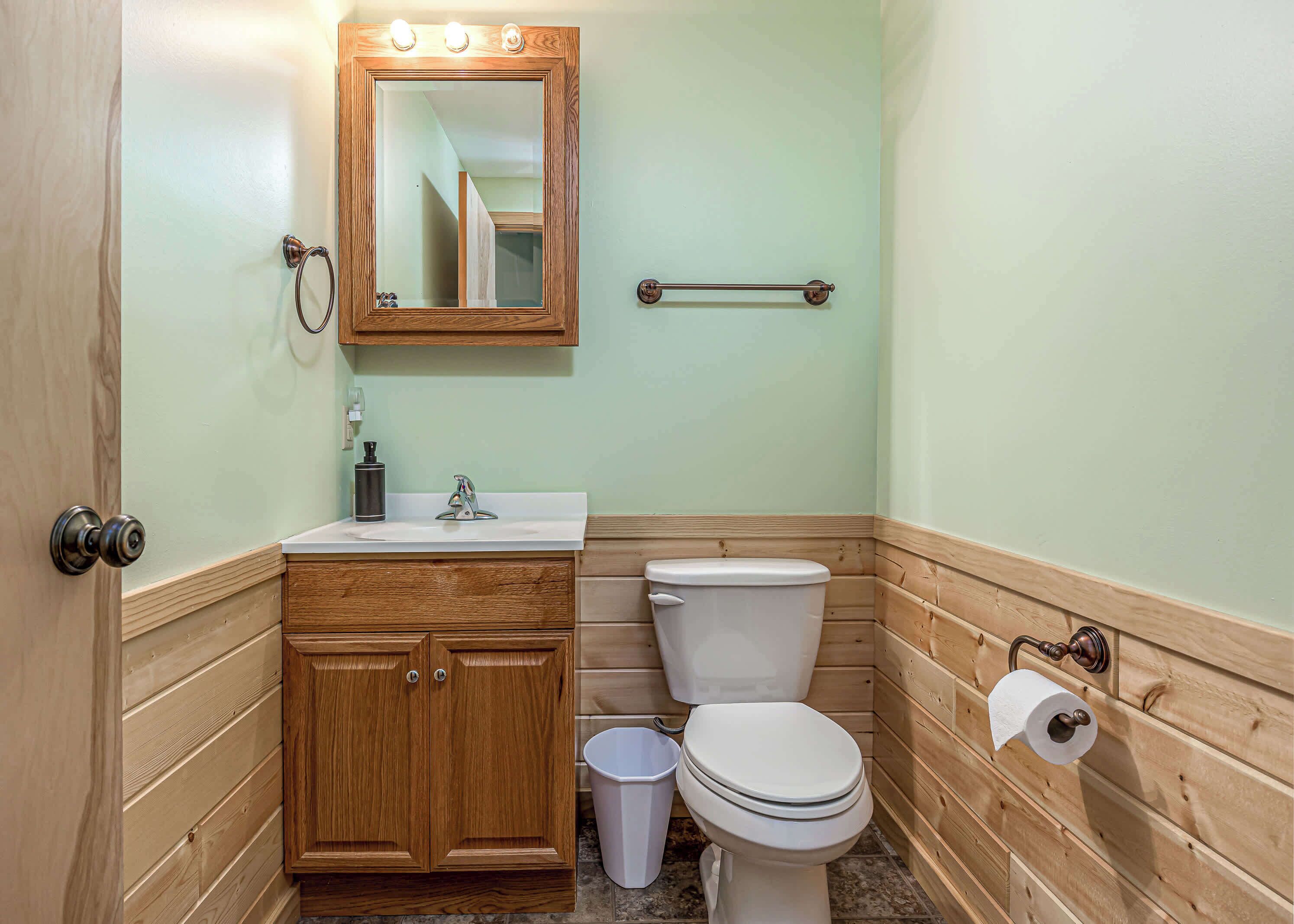 A bathroom with wooden paneling, a white toilet, a sink with a faucet, a mirror, and a towel rack.