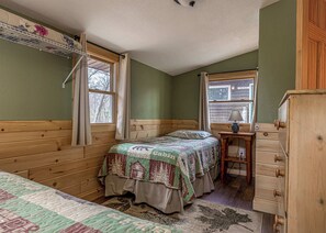 A room with a bed, a dresser, a window with curtains, and a wall-mounted shelf.