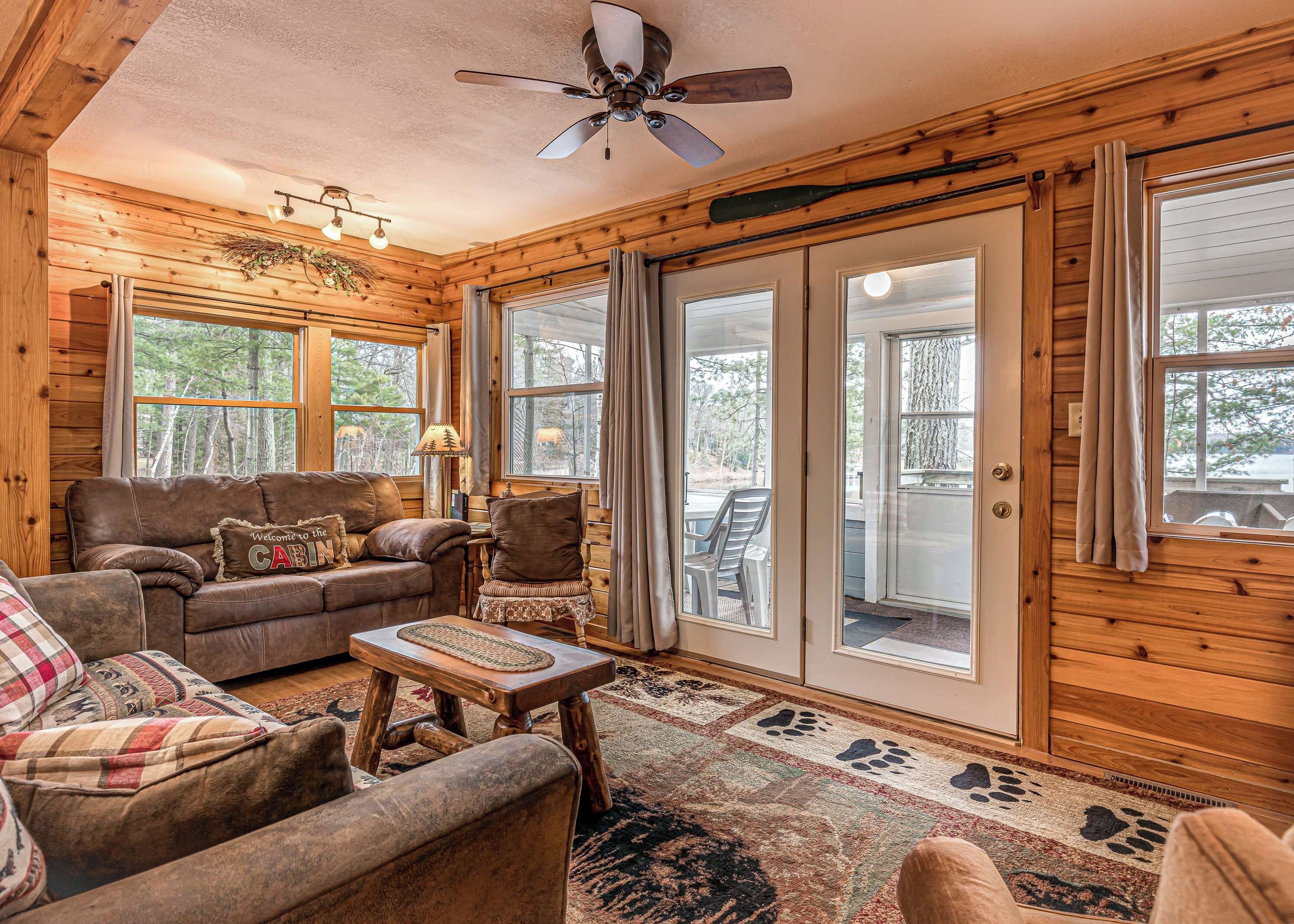 A cozy cabin interior with a wooden interior, a ceiling fan, a sofa, a chair, and a dining table.
