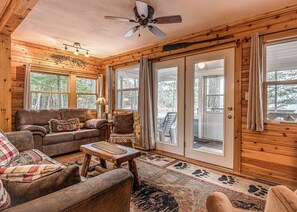 A cozy cabin interior with a wooden interior, a ceiling fan, a sofa, a chair, and a dining table.