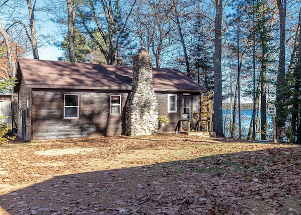 A rustic cabin with a stone chimney, wooden siding, and a porch with a bench.