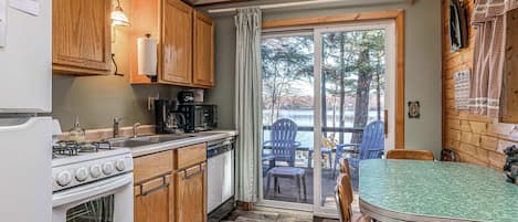 A compact kitchen with a stove, sink, and a view of a lake through a glass door.