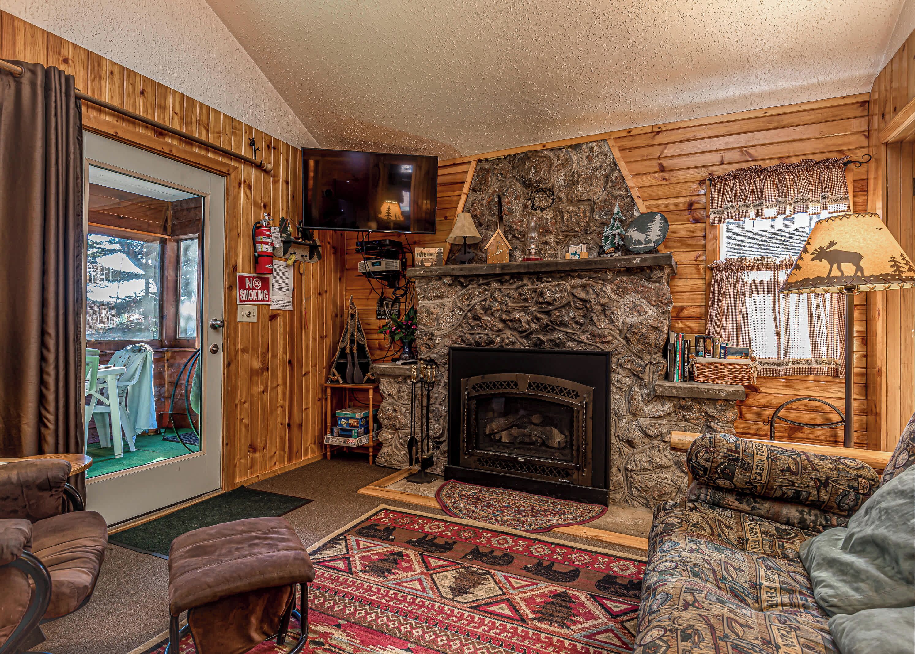 A cozy cabin interior with a stone fireplace, wooden walls, a television, and a dining area.
