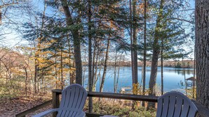 Una terraza con dos sillas Adirondack y una mesita, con vista a un lago tranquilo rodeado de árboles.