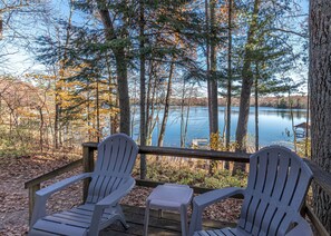 Varanda com duas cadeiras Adirondack e uma pequena mesa, com vista para um lago calmo rodeado por árvores.