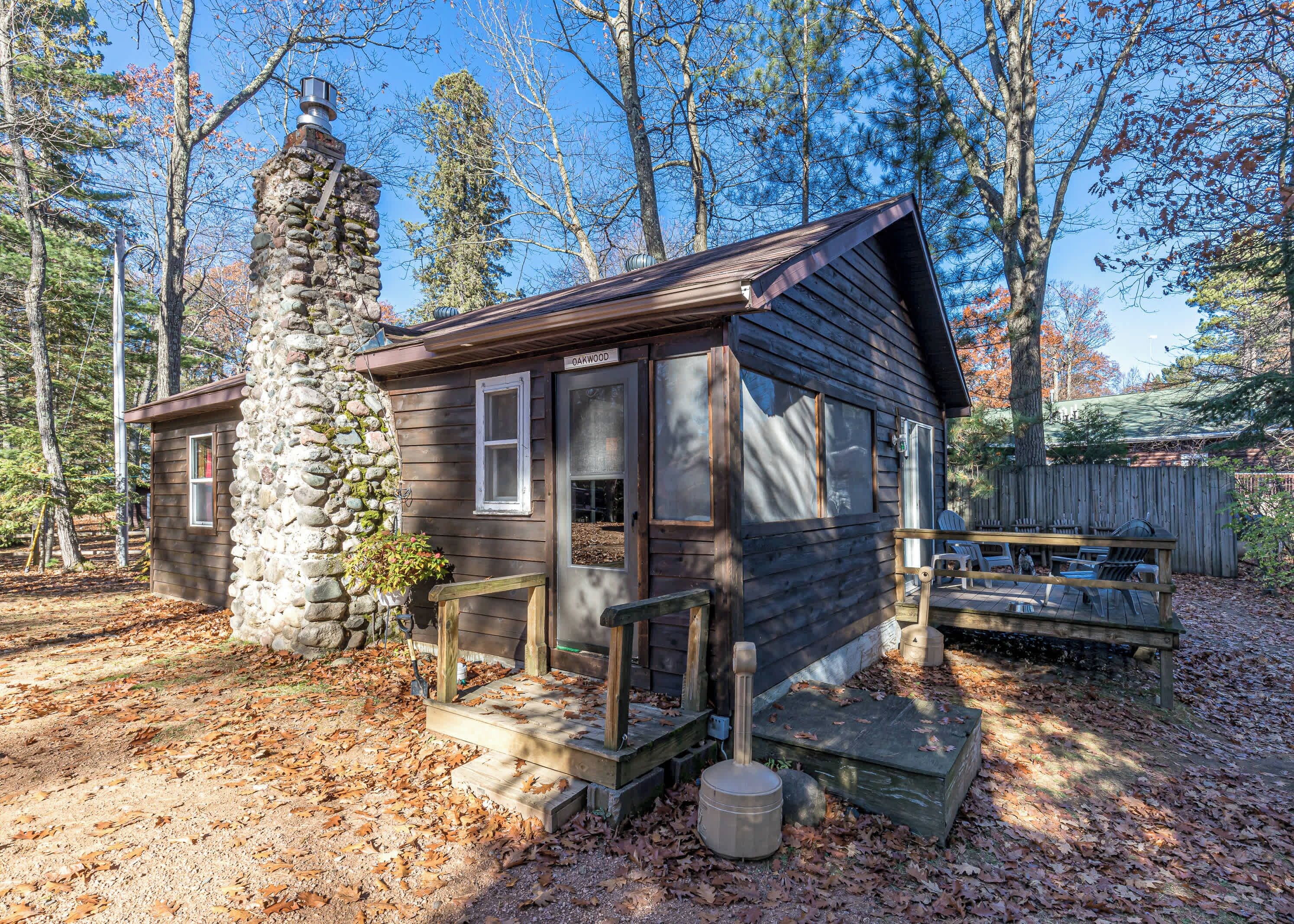 Une cabane rustique avec une cheminée en pierre, une terrasse en bois et un petit porche.