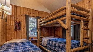 Una habitación tipo cabaña con dos literas, paredes de madera, una ventana con cortinas y una pequeña mesa.