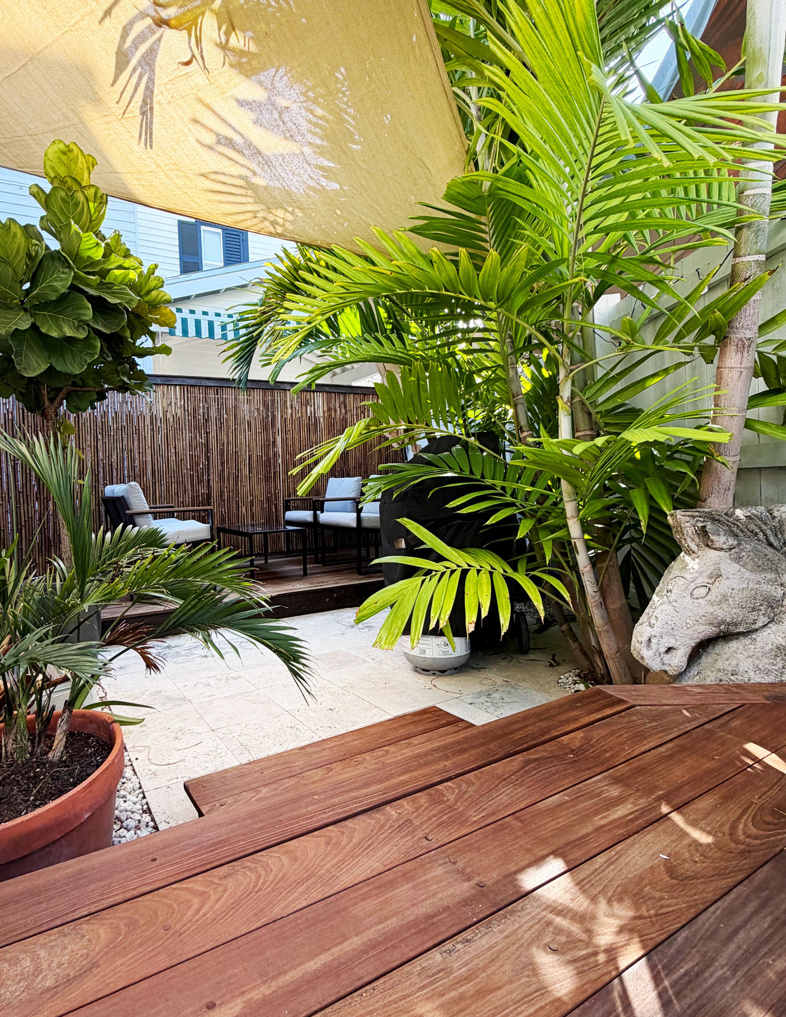 A wooden deck with a table, surrounded by potted plants and a bamboo fence.