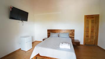 Un dormitorio con una cama, un televisor montado en la pared, un armario de madera y una mesita de noche blanca.