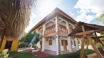 Um edifício de dois andares com varanda, estrutura de telhado de palha e baloiço de madeira.