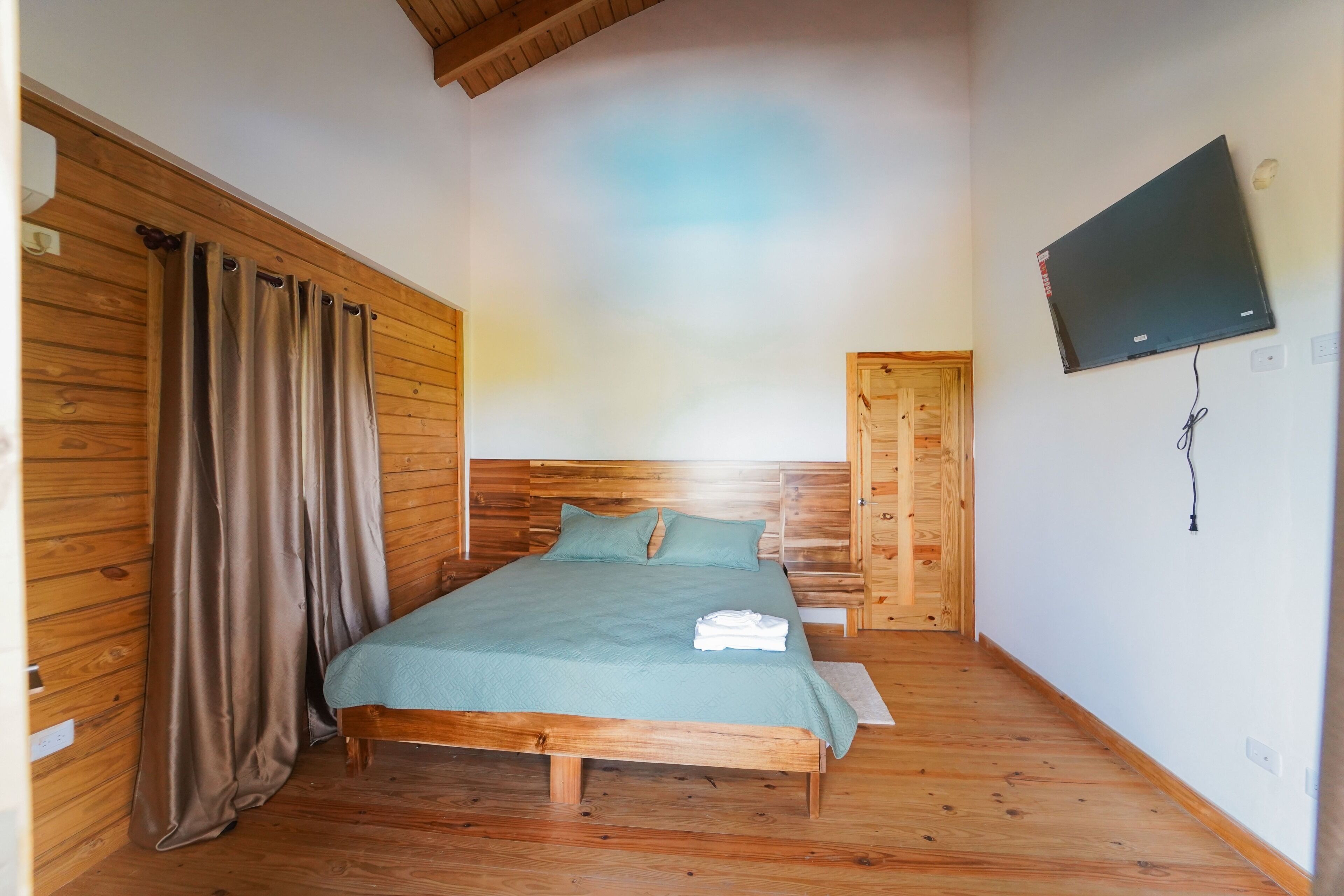 A room with a bed, wooden walls, a television mounted on the wall, and a door.