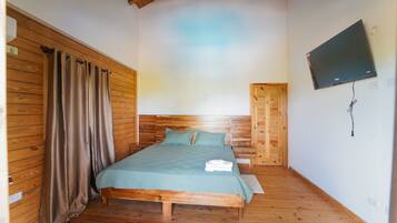 A room with a bed, wooden walls, a television mounted on the wall, and a door.