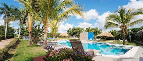A swimming pool with lounge chairs, surrounded by palm trees and a flower bed.