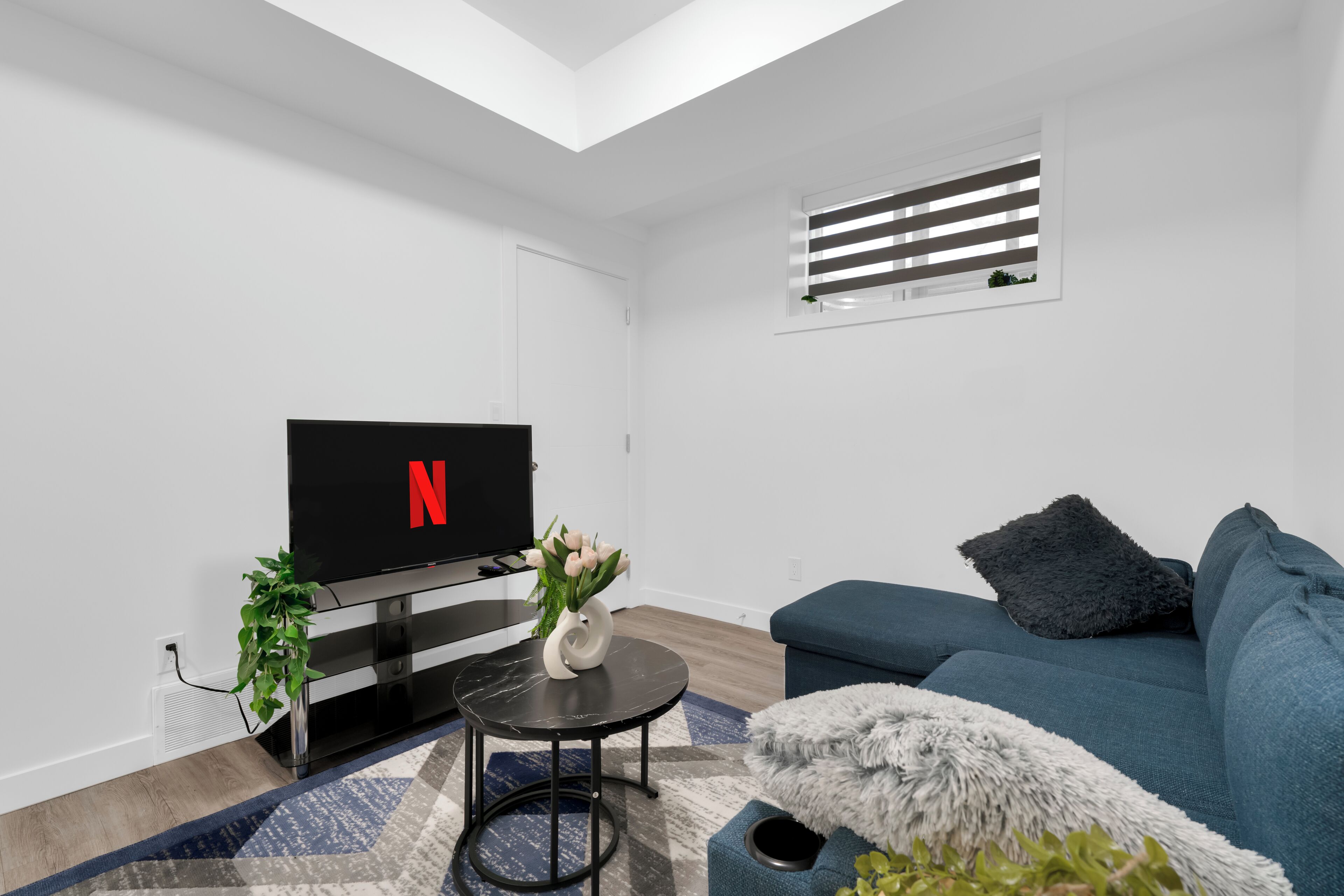 A modern living room with a flat-screen TV, a sofa, a small round table, and a potted plant.