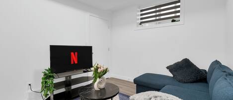 A modern living room with a flat-screen TV, a sofa, a small round table, and a potted plant.