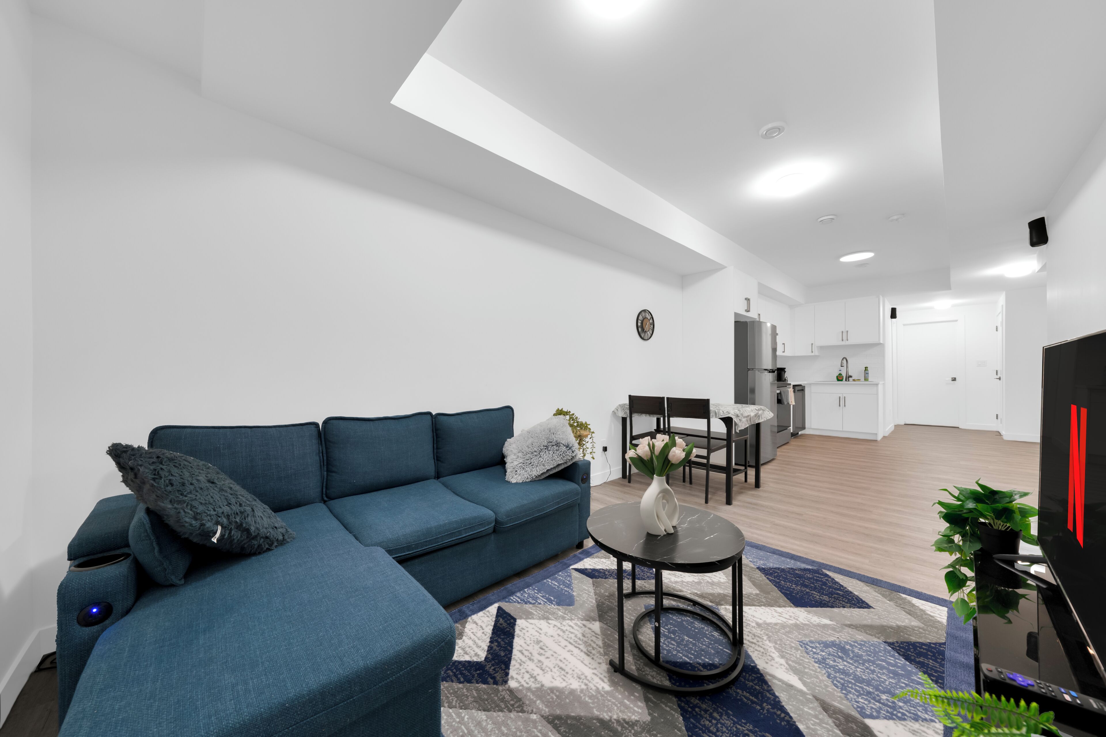 A modern living room with a blue sofa, a round coffee table, and a dining area with a chair and table.