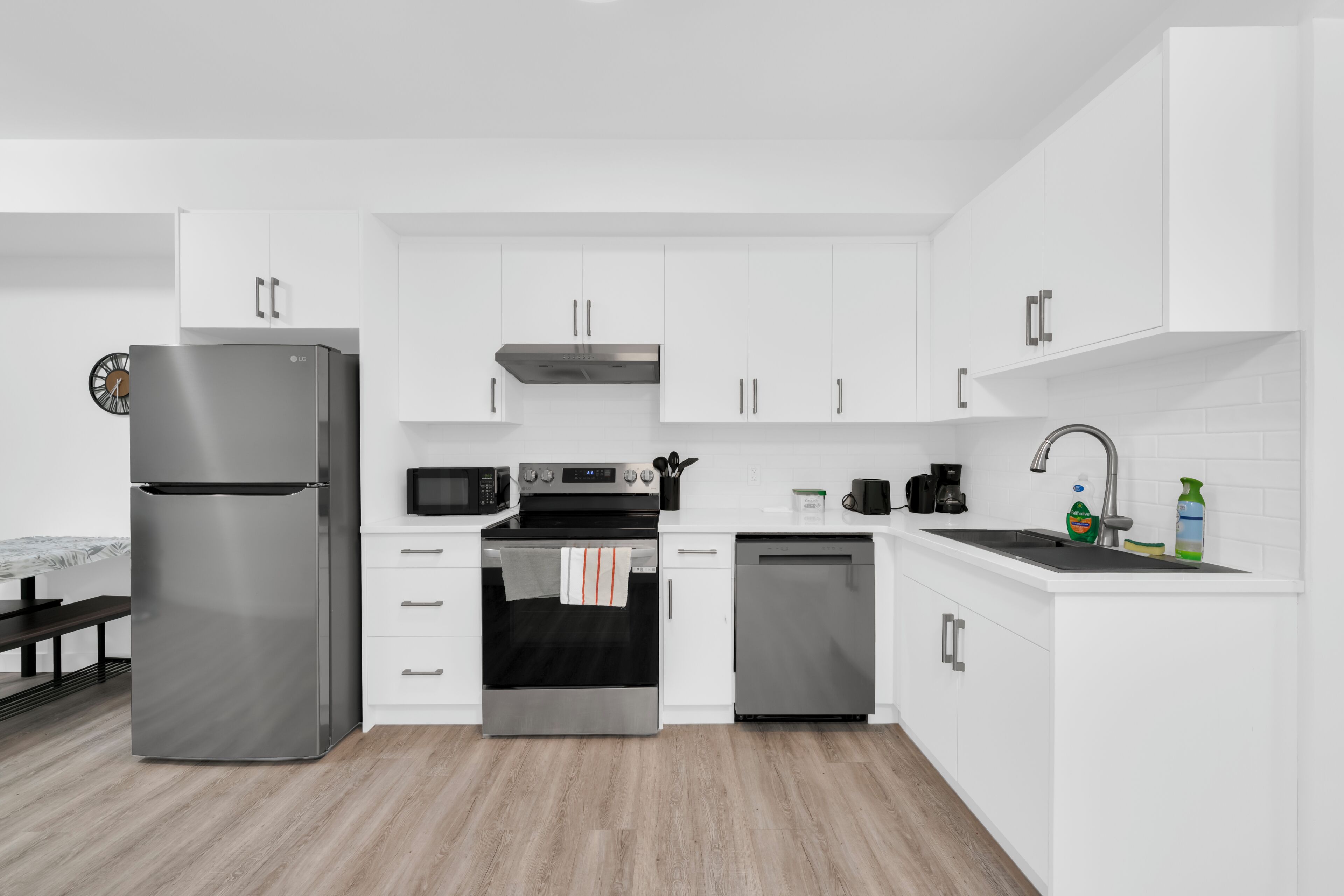 Una cocina moderna con armarios blancos, electrodomésticos de acero inoxidable, microondas, horno, lavavajillas y un lavabo con grifo.