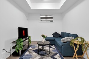 Un salon moderne avec un téléviseur à écran plat, un canapé, une table basse et une petite plante posée sur un support.
