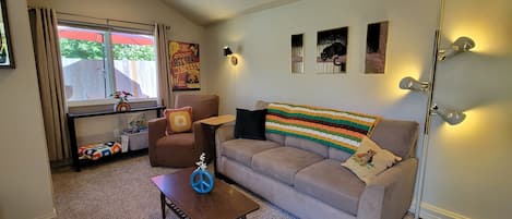 A living room with a sofa, a coffee table, a chair, and a window with curtains.