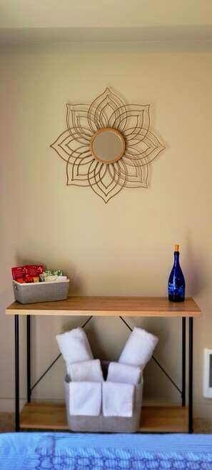 Ein Zimmer mit einem an der Wand befestigten, dekorativen Metallkunstwerk, einem Holztisch mit einer Flasche und einer Kiste sowie einem weißen Stuhl mit einem Handtuch.