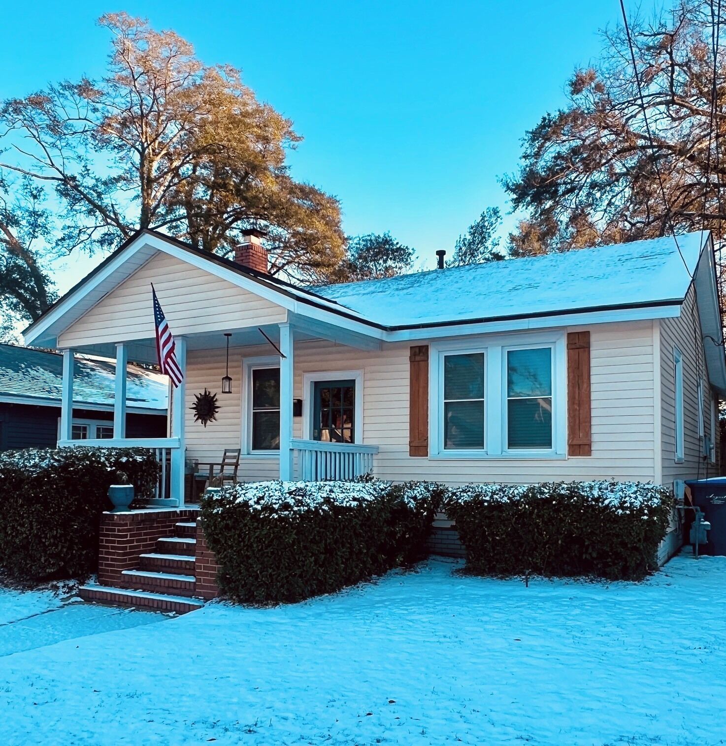 Une maison de plain-pied avec un porche à l’avant, une cheminée et une pelouse recouverte de neige.