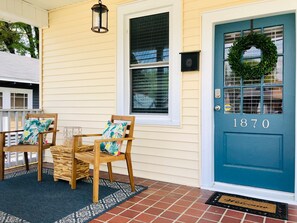A front porch with two wooden chairs, a blue door with the number 1870, and a wreath above the door. - "Music & Martinis" Charming Cottage Near Medical District (Augusta)