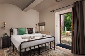 Un dormitorio con cama, mesitas de noche, un radiador y vistas a un jardín a través de una puerta abierta.