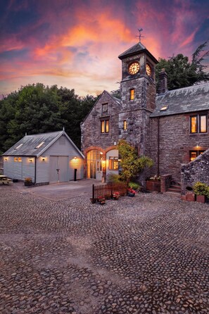 A stone building with a clock tower, a covered patio, and a gravel driveway. - Historic Clocktower House | Spa Barn | Sleeps 12 (Cumberland)