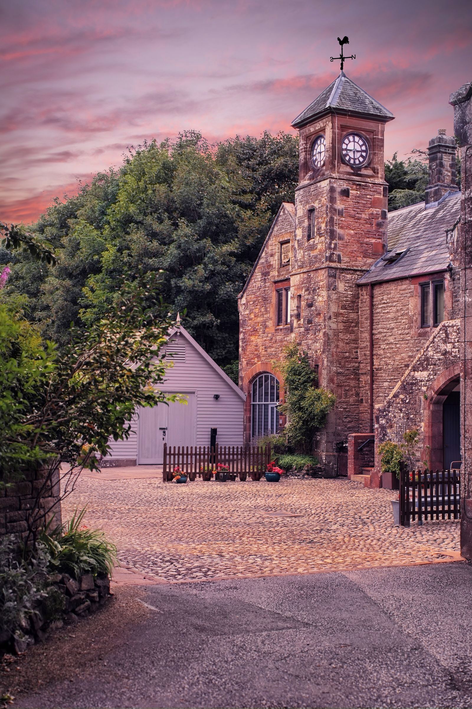 A historic stone building with a clock tower, a covered porch, and a gravel driveway.